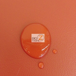 May include: A close-up of a bright orange fabric with a water droplet on it. The fabric has a textured surface. The water droplet is round and clear. The text "BIG Z FABRIC" is visible in the water droplet.
