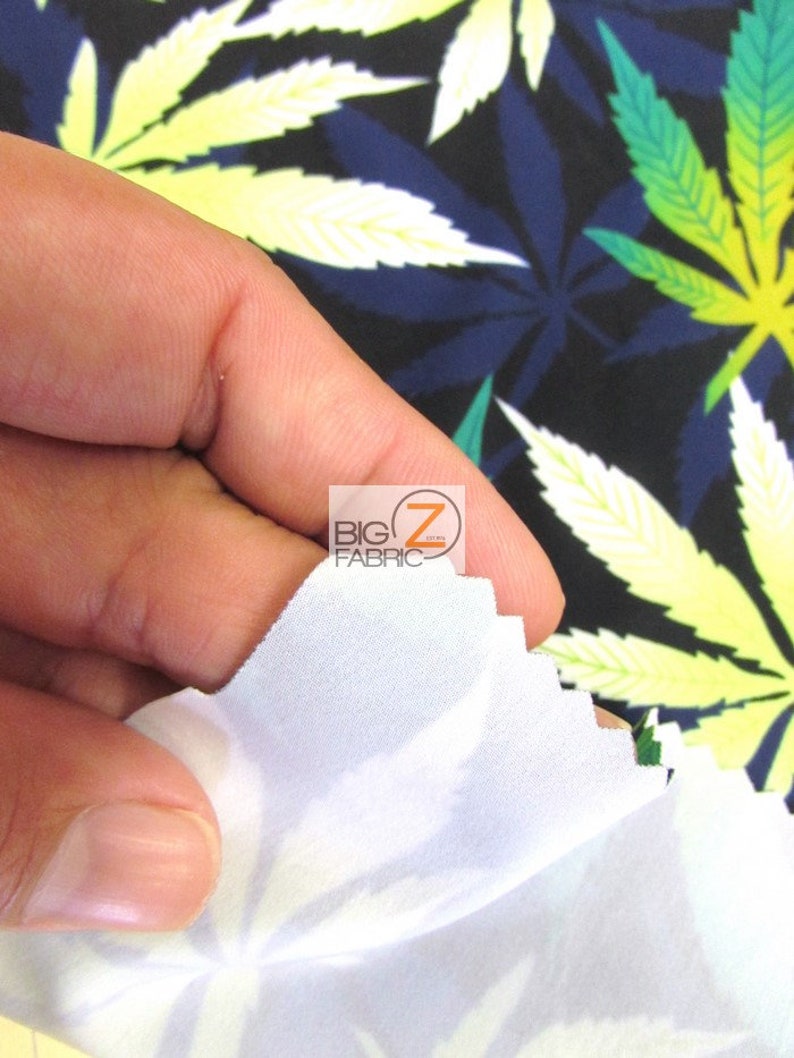 Puede incluir: Primer plano de una tela blanca con un estampado de hojas de marihuana verdes y amarillas. La tela est&aacute; siendo sostenida por una mano, y el estampado es visible en ambos lados de la tela.