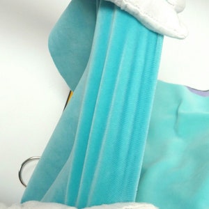 May include: Close-up of a light blue velvet fabric, held by white-gloved hands. The fabric is draped, showing its texture and colour. The image highlights the softness and sheen of the material, suggesting a luxurious textile.