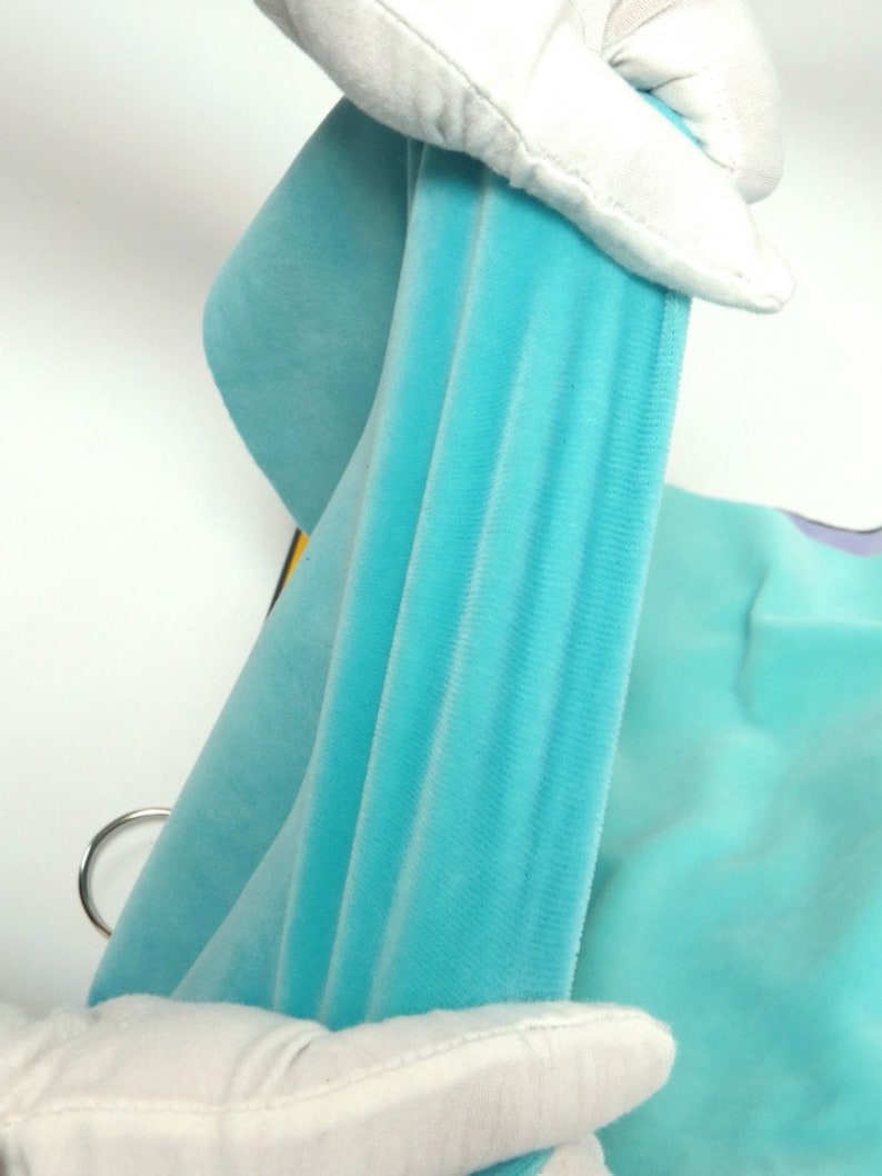 May include: Close-up of a light blue velvet fabric, held by white-gloved hands. The fabric is draped, showing its texture and colour. The image highlights the softness and sheen of the material, suggesting a luxurious textile.