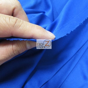 Puede incluir: Primer plano de una tela azul real brillante. La tela es lisa y tiene un ligero brillo. La tela est&aacute; siendo sostenida por una mano, y los bordes est&aacute;n ligeramente deshilachados.