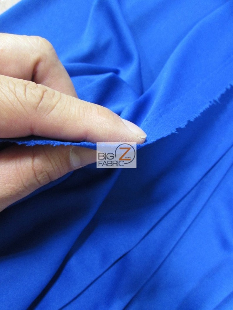 Puede incluir: Primer plano de una tela azul real brillante. La tela es lisa y tiene un ligero brillo. La tela est&aacute; siendo sostenida por una mano, y los bordes est&aacute;n ligeramente deshilachados.