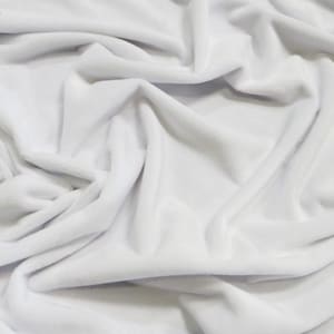 May include: White plush fabric with a soft, velvety texture. The fabric is folded and draped, showcasing its smooth surface and subtle sheen.