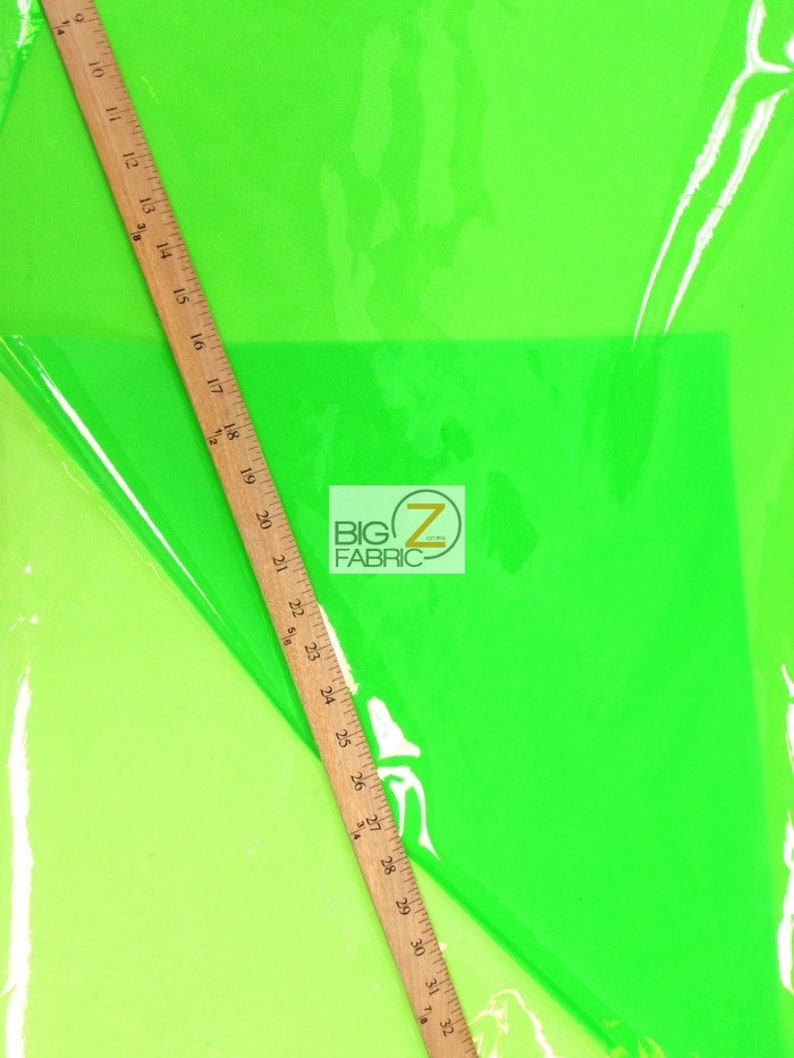 Puede incluir: Tela verde ne&oacute;n brillante con una regla de madera en diagonal. La regla mide hasta 81 cm. La tela tiene un aspecto brillante y transparente. El logotipo "BIG Z FABRIC" es visible.