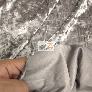 May include: Close-up of a silver crushed velvet fabric with a subtle sheen. The fabric is soft and luxurious, with a slightly textured surface. The fabric is folded in half, revealing the back side, which is a smooth, satin-like material.