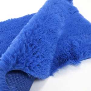 May include: A close-up of a bright blue faux fur rug. The rug is folded in half, showing the soft, plush texture of the fur. The underside of the rug is a matching blue fabric.