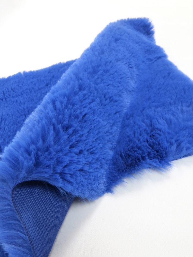 May include: A close-up of a bright blue faux fur rug. The rug is folded in half, showing the soft, plush texture of the fur. The underside of the rug is a matching blue fabric.