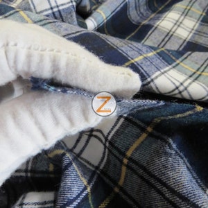 May include: Close-up of a blue and white plaid fabric with a yellow stripe. The fabric is folded and the edges are frayed.