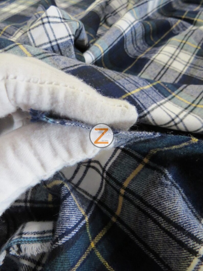 May include: Close-up of a blue and white plaid fabric with a yellow stripe. The fabric is folded and the edges are frayed.