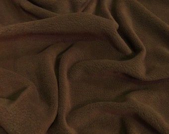 May include: A close-up of a brown fleece fabric with a soft, fuzzy texture. The fabric is folded and draped, showing its drapability and warmth.