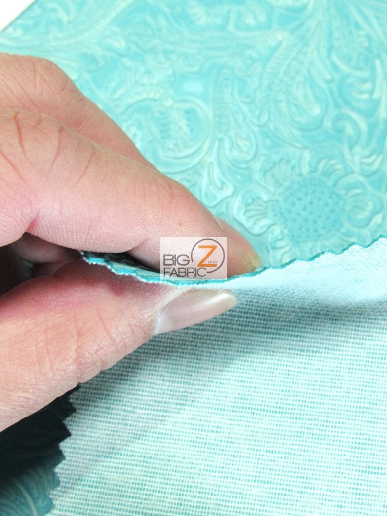 May include: Close-up of turquoise blue embossed fabric with a floral pattern. The fabric is being held in a hand, showing the back side of the fabric, which is a plain turquoise blue.