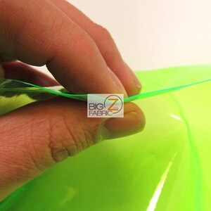 Puede incluir: Primer plano de una mano tocando una l&aacute;mina de tela verde ne&oacute;n brillante. La tela es transl&uacute;cida y refleja la luz. El logotipo "BIG Z FABRIC" es visible en la esquina.