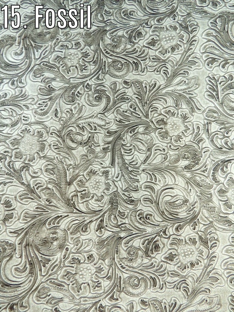 May include: A close-up of a silver embossed fabric with a floral pattern. The fabric has a textured, raised design.