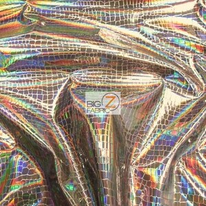 May include: A close-up of iridescent fabric with a crocodile skin pattern. The fabric has a shimmering, holographic effect with shades of gold, blue, green, and purple.