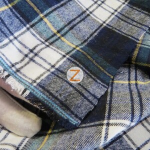 May include: Close-up of a blue, white, and yellow plaid fabric with a frayed edge. The fabric is folded over itself, creating a layered effect.