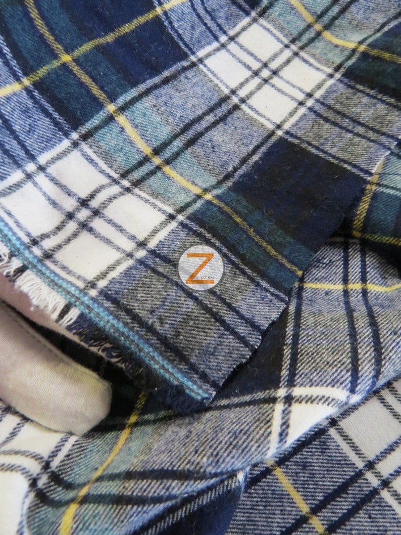 May include: Close-up of a blue, white, and yellow plaid fabric with a frayed edge. The fabric is folded over itself, creating a layered effect.