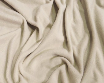 Puede incluir: Primer plano de una tela de franela suave de color beige con una textura lisa. La tela está drapeada y doblada, creando un aspecto suave y acogedor.