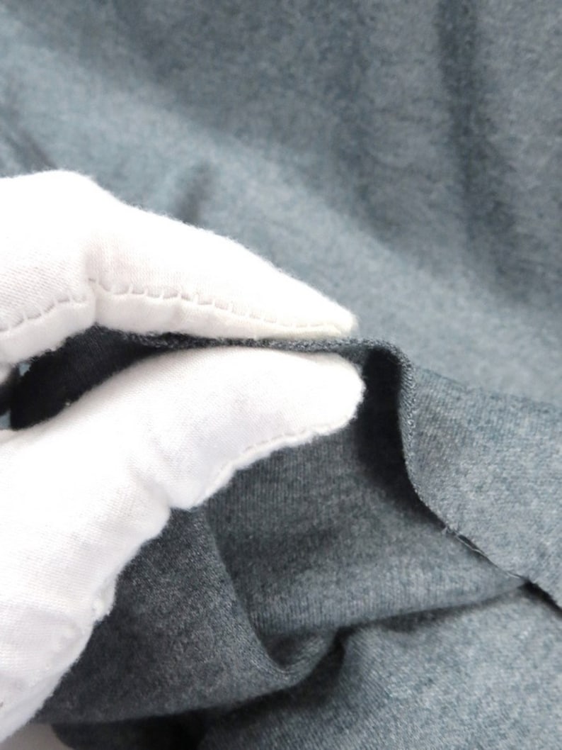 May include: Close-up of a dark gray fabric with a soft, textured surface. The fabric is folded and held by a white gloved hand.
