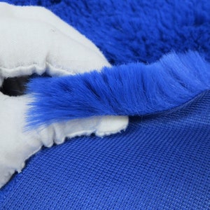 May include: Close-up of a blue faux fur fabric with a white backing. The fur is soft and fluffy, and the backing is smooth and white.