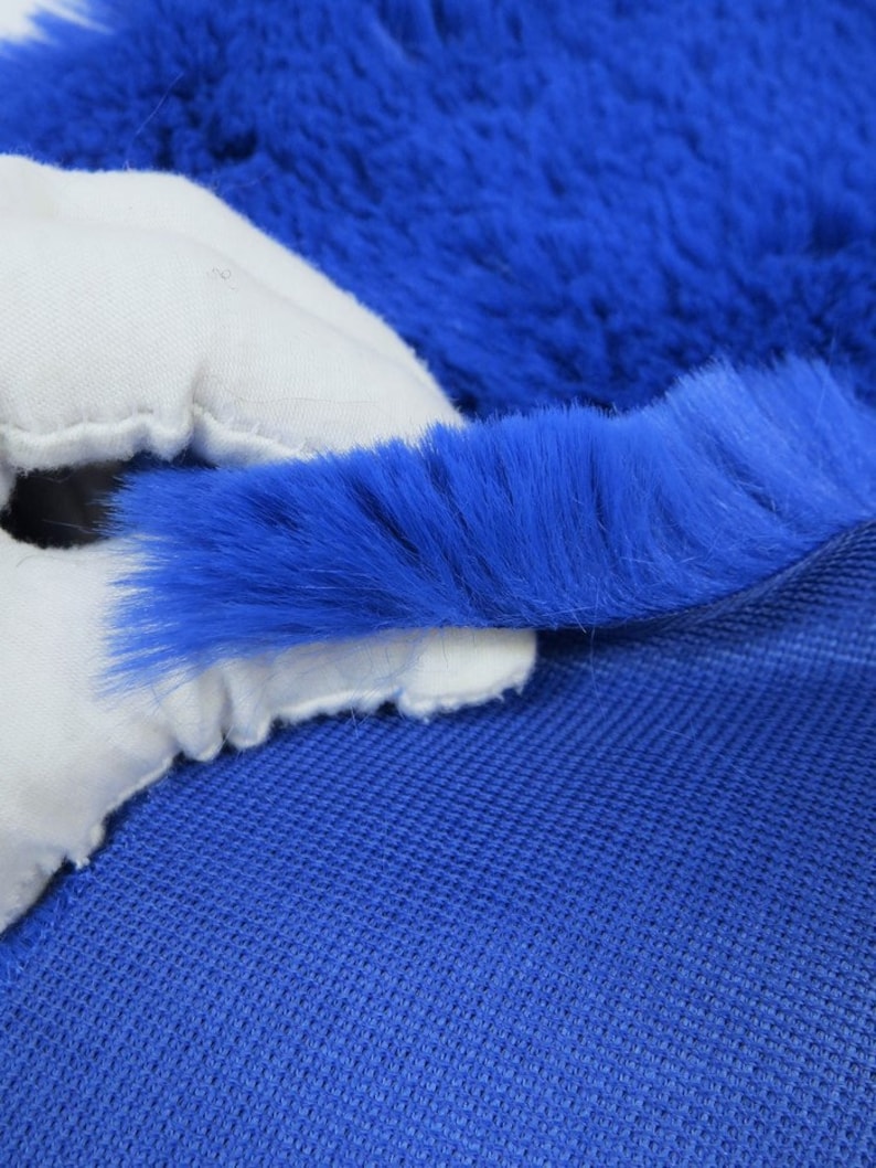 May include: Close-up of a blue faux fur fabric with a white backing. The fur is soft and fluffy, and the backing is smooth and white.