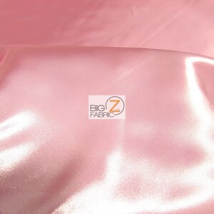 May include: Close-up of a pink satin fabric with a smooth, shiny surface. The fabric is folded, creating soft shadows and highlights. The Big Z Fabric logo is visible in the corner.