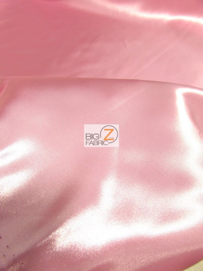 May include: Close-up of a pink satin fabric with a smooth, shiny surface. The fabric is folded, creating soft shadows and highlights. The Big Z Fabric logo is visible in the corner.