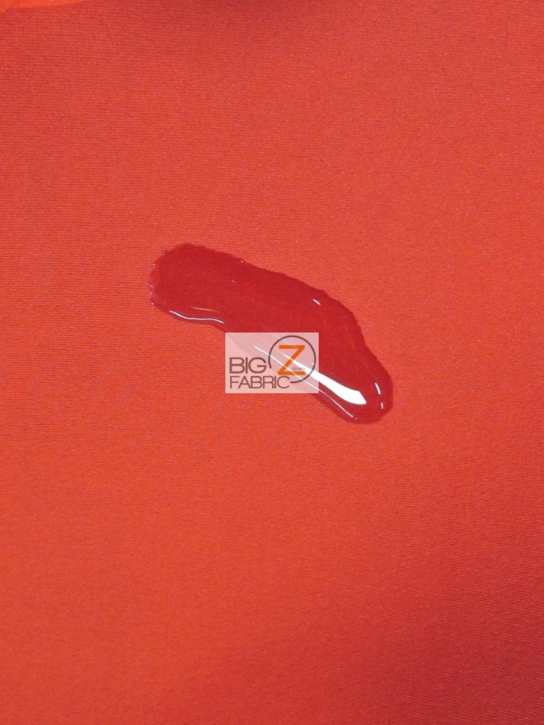 May include: A close-up of a bright orange fabric with a water droplet on it. The fabric is smooth and has a slight sheen. The water droplet is clear and round. The text "BIG Z FABRIC" is visible in the lower center of the image.