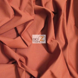 May include: Close-up of a rust-colored fabric with a smooth texture. The fabric is folded and draped, showing its soft and flowing nature.