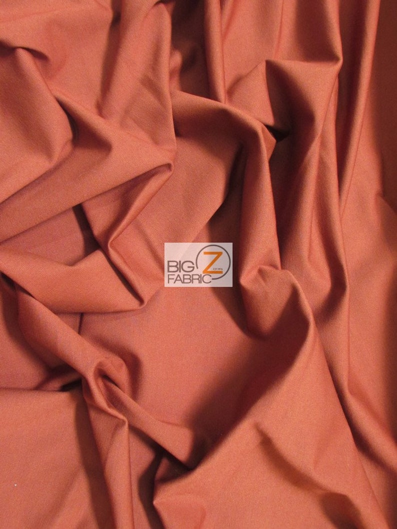 May include: Close-up of a rust-colored fabric with a smooth texture. The fabric is folded and draped, showing its soft and flowing nature.