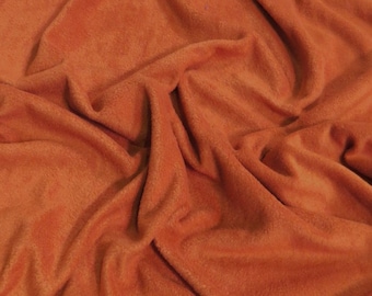 May include: A close-up of a soft, orange fleece fabric with a textured surface. The fabric is folded and draped, creating a soft and inviting look.