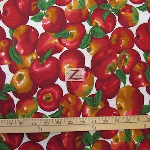 May include: White fabric with a repeating pattern of red apples with green leaves. The fabric is measured with a wooden ruler.