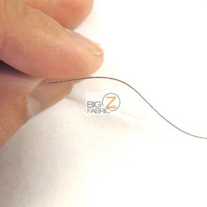 Peut inclure: Gros plan sur une feuille de plastique transparente, mince et flexible avec un fil brun qui la traverse. La feuille est tenue par un doigt.