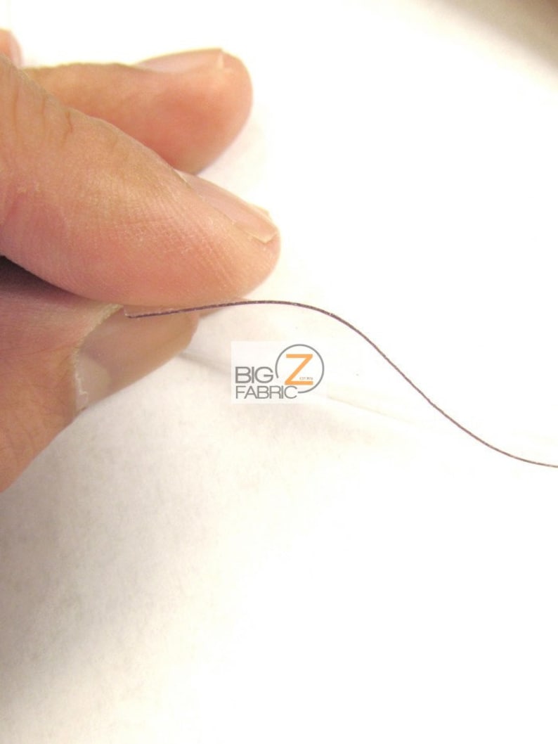 Peut inclure: Gros plan sur une feuille de plastique transparente, mince et flexible avec un fil brun qui la traverse. La feuille est tenue par un doigt.
