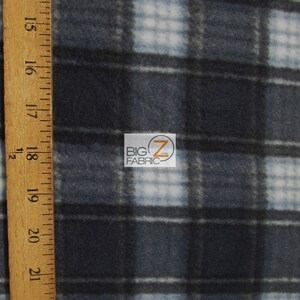 May include: Close-up of a blue and white plaid fleece fabric. The fabric is soft and fuzzy, and it has a subtle sheen. The plaid pattern is made up of thin white lines and thicker blue lines. The fabric is measured with a wooden ruler.