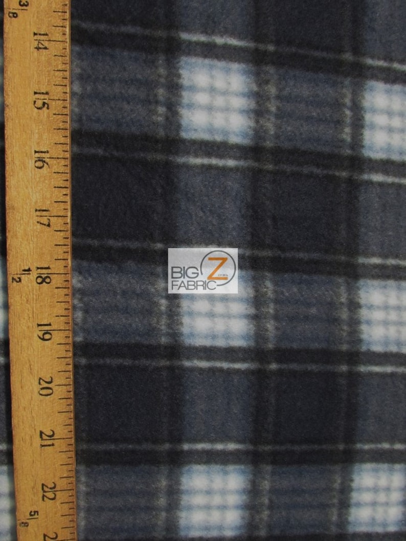 May include: Close-up of a blue and white plaid fleece fabric. The fabric is soft and fuzzy, and it has a subtle sheen. The plaid pattern is made up of thin white lines and thicker blue lines. The fabric is measured with a wooden ruler.
