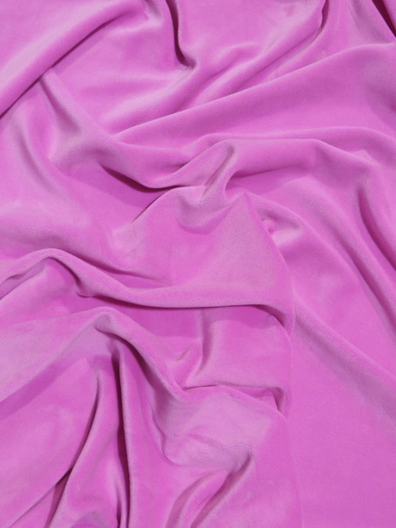 May include: A close-up of a bright pink fabric, possibly velvet, with a soft, flowing texture. The material is draped and folded, creating shadows and highlights. The folds and creases add depth and visual interest to the image, highlighting the fabric's luxurious appearance.
