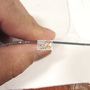 Peut inclure: Gros plan sur une feuille de plastique transparente et flexible avec un bord de paillettes argent&eacute;es. La feuille est tenue par une main.