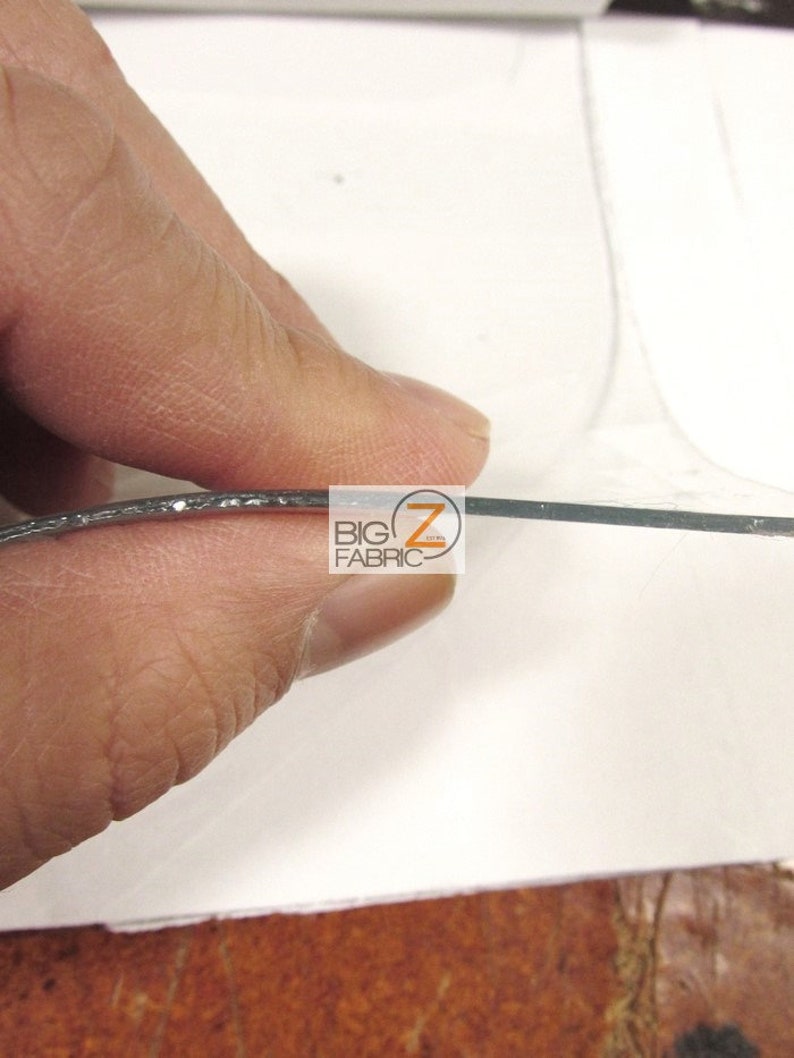 Peut inclure: Gros plan sur une feuille de plastique transparente et flexible avec un bord de paillettes argent&eacute;es. La feuille est tenue par une main.