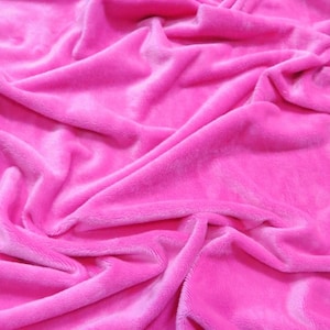 May include: A close-up of a soft, pink fabric with a smooth, velvety texture. The fabric is draped and folded, creating a luxurious and inviting look.