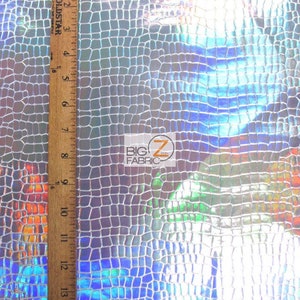 May include: Close-up of iridescent silver fabric with a crocodile skin pattern. The fabric is textured and has a slight sheen. A ruler is visible on the left side of the image, measuring up to 15 inches.