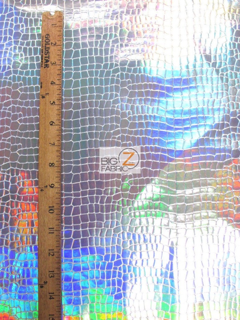 May include: Close-up of iridescent silver fabric with a crocodile skin pattern. The fabric is textured and has a slight sheen. A ruler is visible on the left side of the image, measuring up to 15 inches.