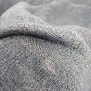 May include: Close-up of a soft, textured, blue fabric. The fabric has a slightly mottled appearance, suggesting a blend of fibers.