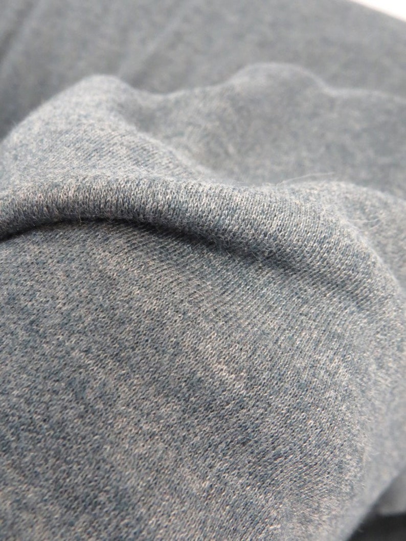 May include: Close-up of a soft, textured, blue fabric. The fabric has a slightly mottled appearance, suggesting a blend of fibers.