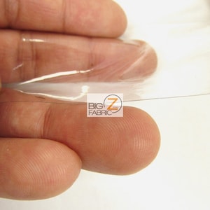 Peut inclure: Gros plan sur une feuille de plastique transparente tenue entre deux doigts. La feuille est fine et flexible, et l&eacute;g&egrave;rement translucide. La feuille est tenue &agrave; la lumi&egrave;re, et la lumi&egrave;re la traverse.