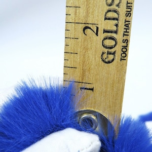 May include: A close-up of a blue faux fur fabric measured with a wooden ruler. The ruler is marked with the number "2" and the text "Goldstrike Tools That Suit Your Needs".