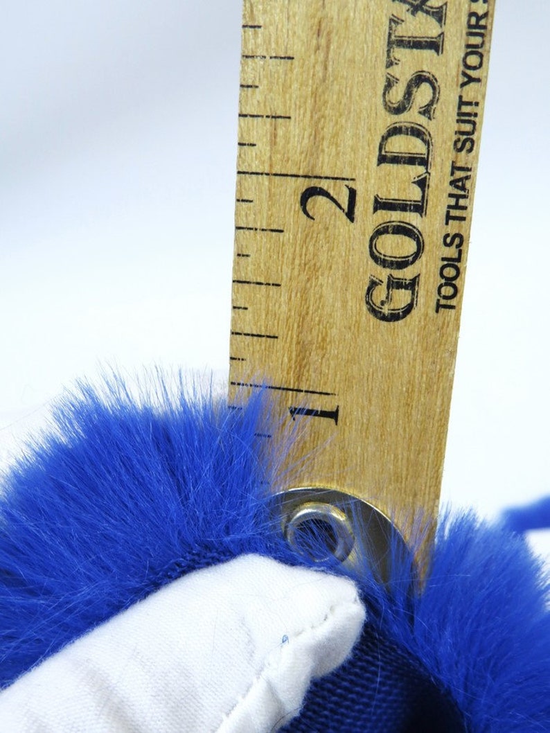 May include: A close-up of a blue faux fur fabric measured with a wooden ruler. The ruler is marked with the number "2" and the text "Goldstrike Tools That Suit Your Needs".