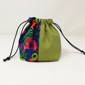 Peut inclure: Un sac à cordon vert et floral avec des cordons noirs. Un côté du sac est de couleur vert unie, et l'autre côté présente un motif floral coloré sur un fond bleu foncé.