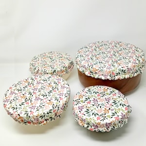 Peut inclure: Ensemble de quatre couvercles de bol réutilisables en silicone avec un motif floral dans des tons de rose, vert et marron. Les couvercles sont faits d'un matériau extensible et peuvent être utilisés pour couvrir des bols de différentes tailles.
