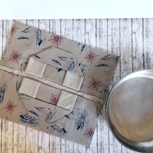 May include: A beige fabric box with a compass design and a white fabric lining. The box is folded open to reveal the interior. The box is sitting on a white wooden surface.
