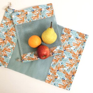 Op de afbeelding: Een blauwe en witte mesh-tas voor producten met een oranje en blauwe bloemenprint stoffen rand. De tas is gevuld met een peer, een sinaasappel en een appel.